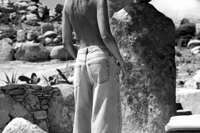 SABURO JEANS Eine Person in hellen Jeans steht vor einem großen Felsen in einer Naturumgebung.