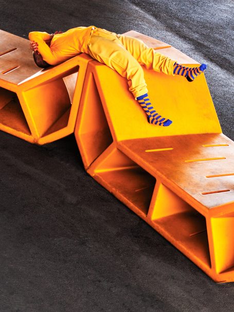 DILLY SOCKS Eine Person in orange Kleidung liegt entspannt auf orangefarbenen, geometrischen Möbeln.
